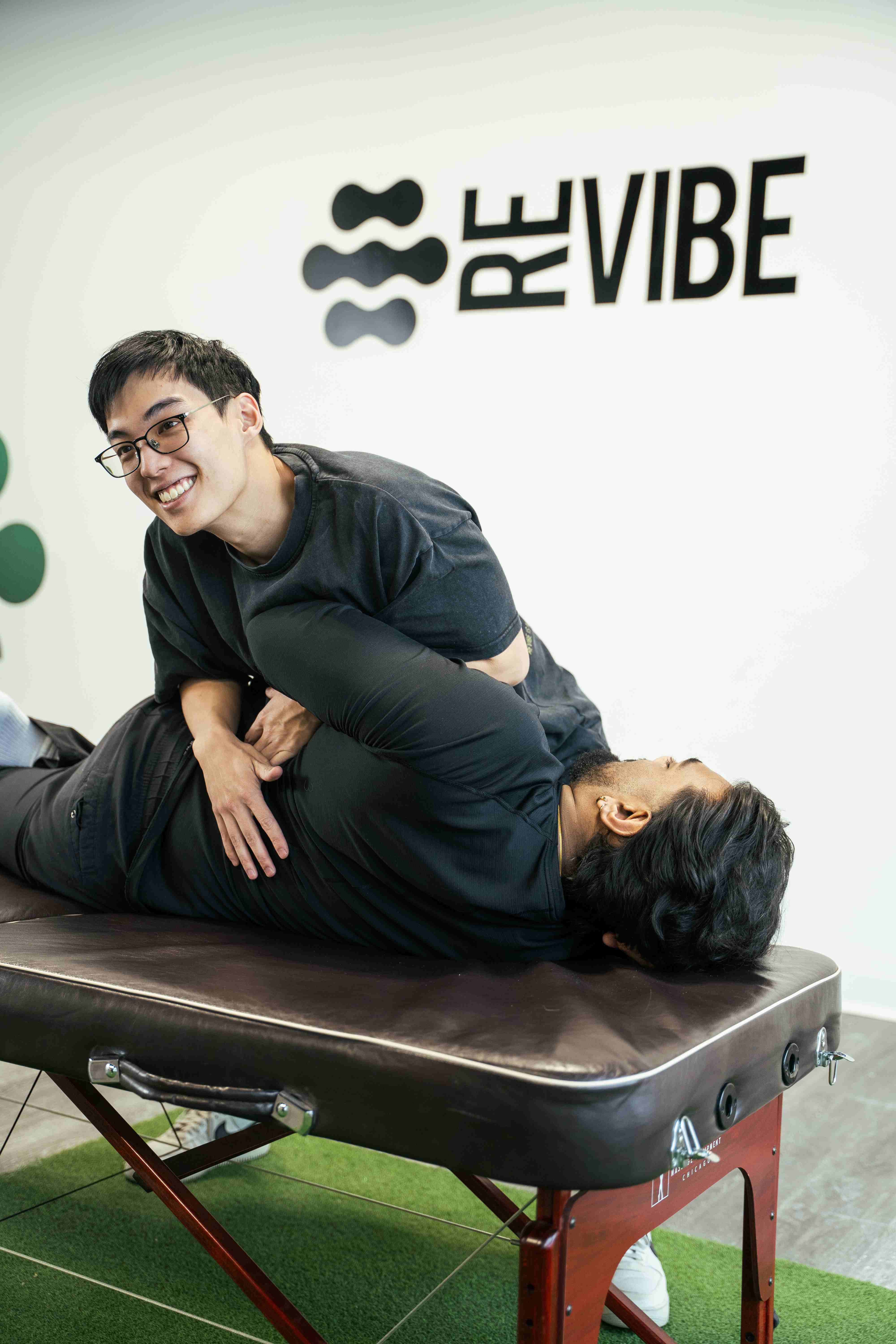 A smiling chiropractor performing a manual back adjustment on a patient.